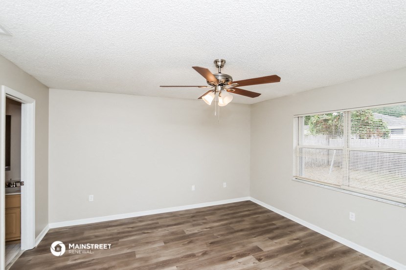 the spacious living room with a large window and a ceiling fan