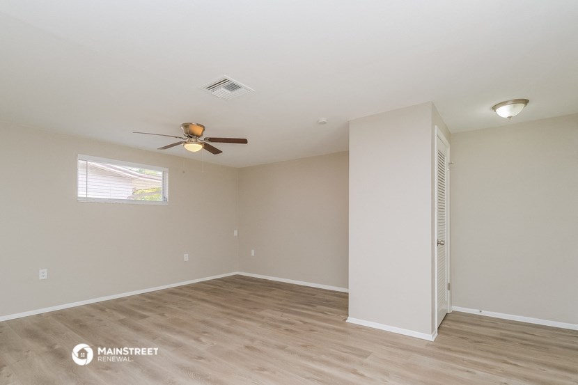 the spacious living room with wood flooring and a ceiling fan