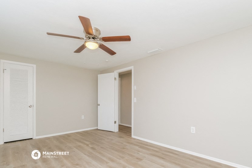 the spacious living room with ceiling fan and white walls