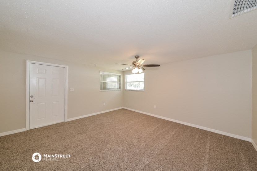 the spacious living room with ceiling fan and carpeting