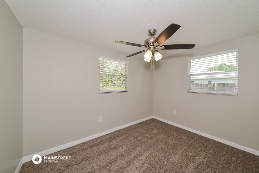 the spacious living room has a ceiling fan and two windows