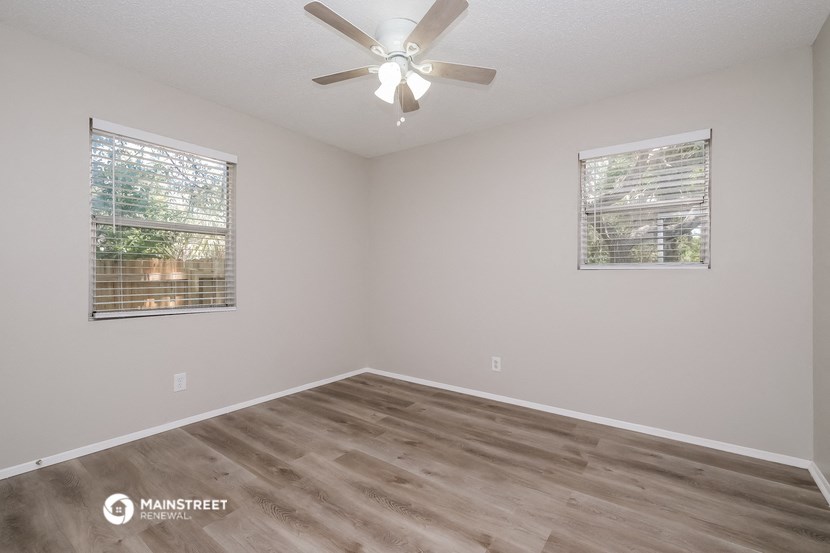 the spacious living room has a ceiling fan and two windows