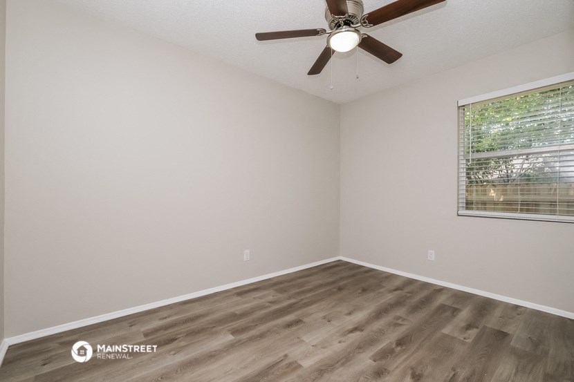 the spacious living room with wood flooring and a ceiling fan