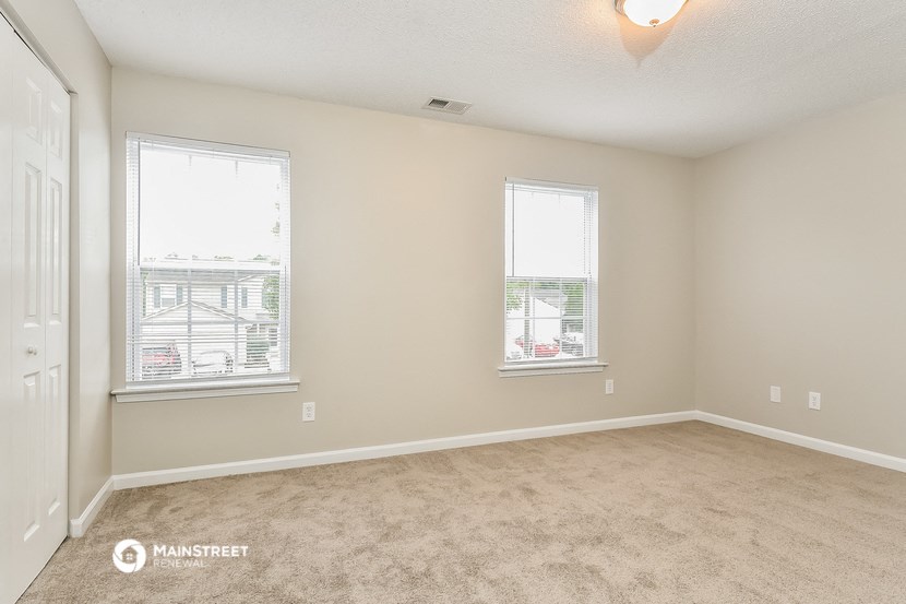 an empty living room with two windows and carpeting