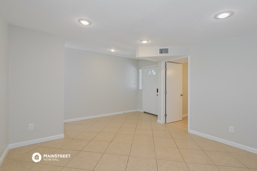 the living room of an apartment with a tiled floor and white walls