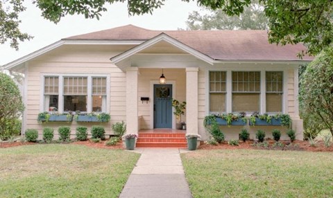A small house with a blue door and windows with green plants on the windowsill.