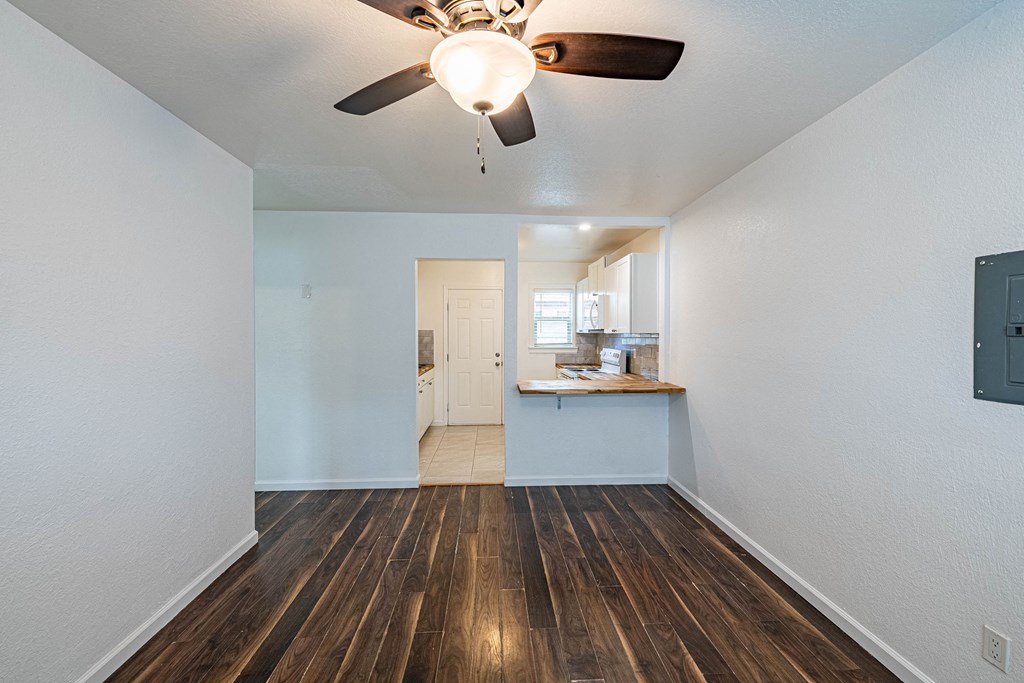 an empty living room with a ceiling fan and a kitchen