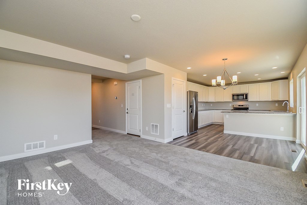 an empty living room and kitchen with white cabinets and wood flooring