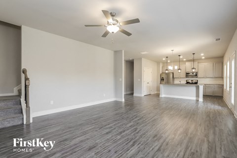 A spacious living room with a kitchen in the background and a staircase on the left.