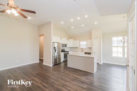 A spacious kitchen and living room with a ceiling fan and wooden floors.