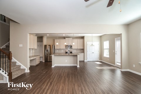 A spacious kitchen and living room with wood flooring and a staircase on the left.