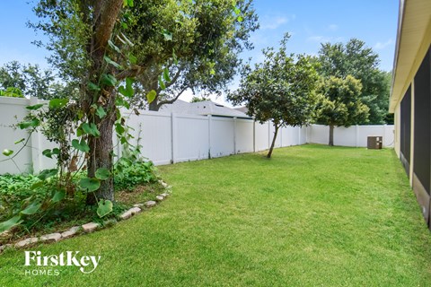 a backyard with grass and trees and a white fence