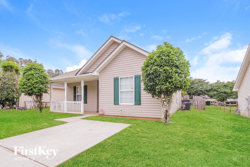 a beige house with green shutters and a lawn and a sidewalk