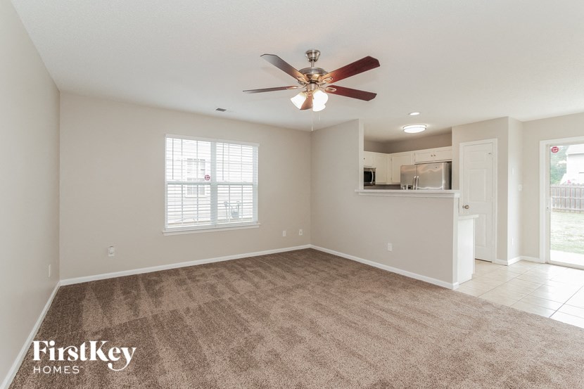 an empty living room with a ceiling fan and a kitchen