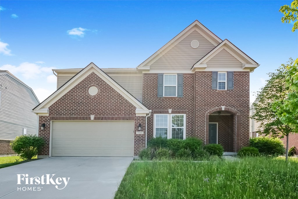 A brick house with a garage door and a tree in front.