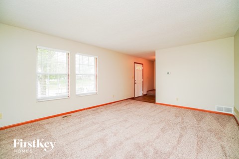 a spacious living room with carpet and two windows