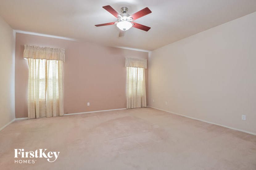 A room with a ceiling fan and two windows with curtains.