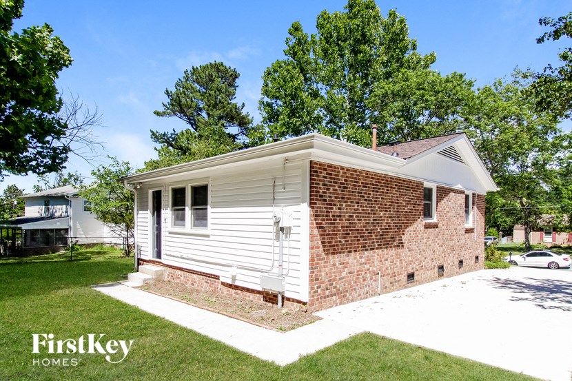 a small white and brick house with a yard and a driveway