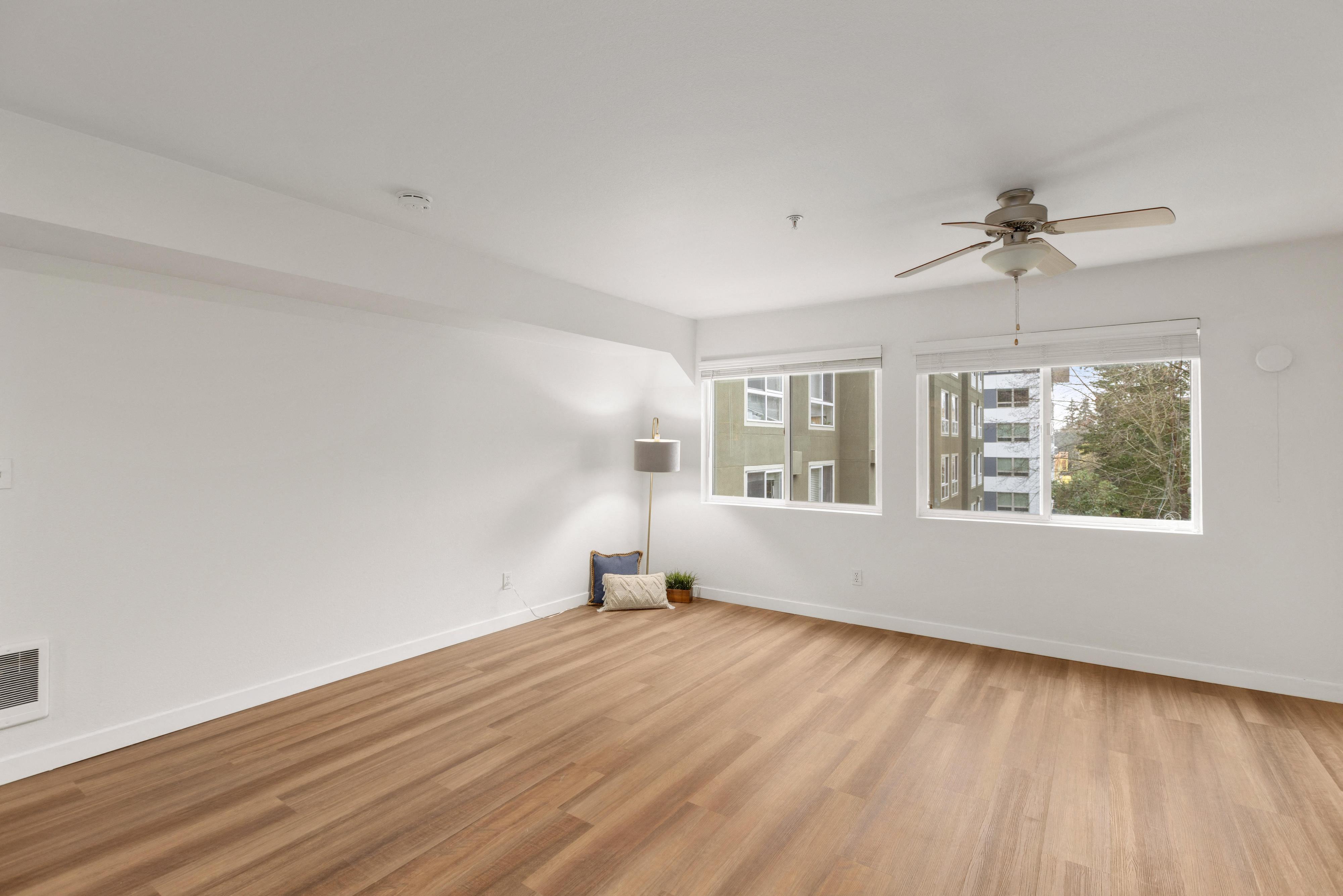 a living room with white walls and wood floors and a ceiling fan
