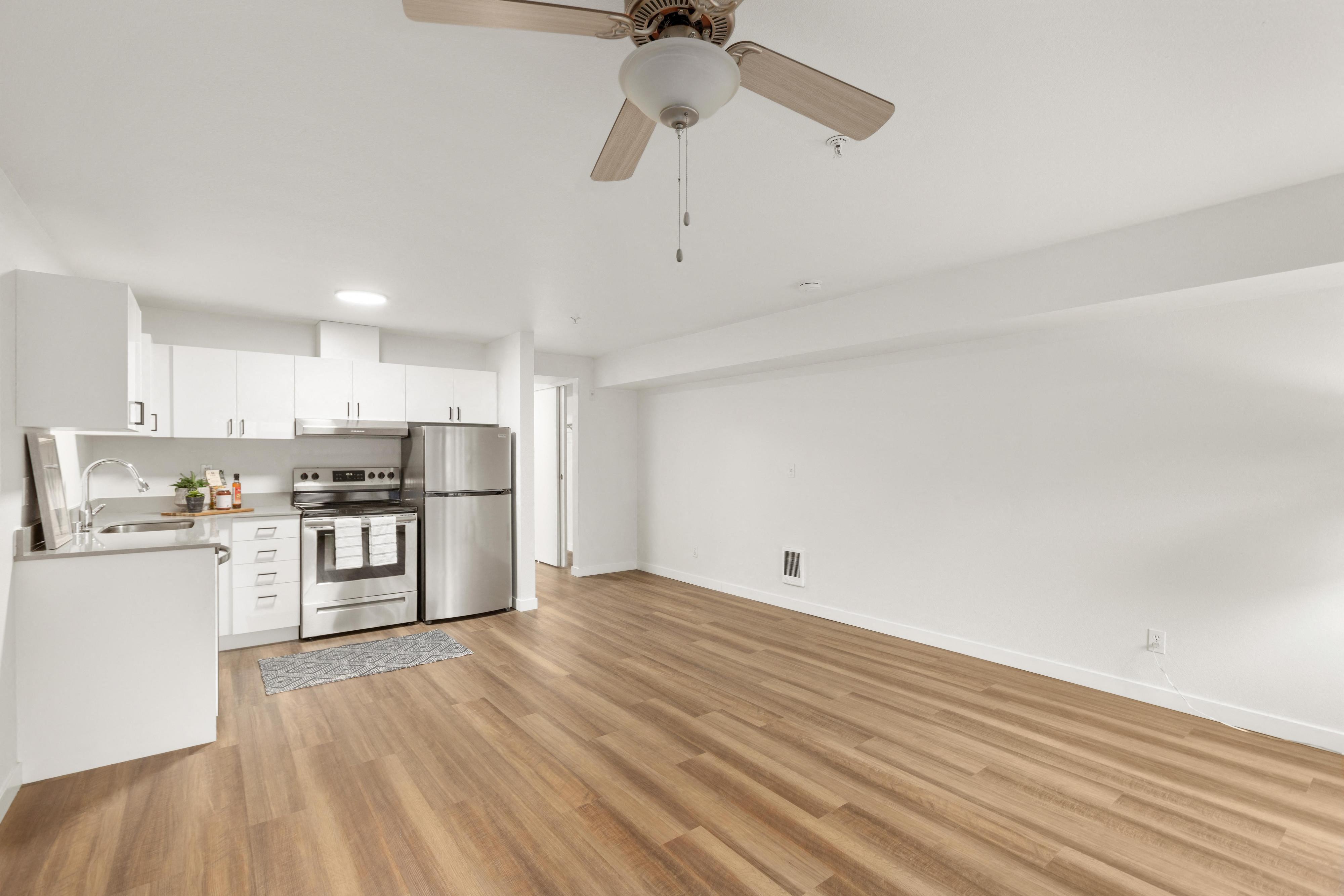 an empty living room with a ceiling fan and a kitchen