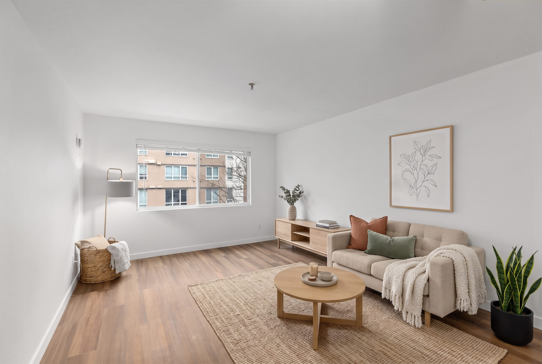 A living room with a couch, a coffee table, and a window with a view of a building.
