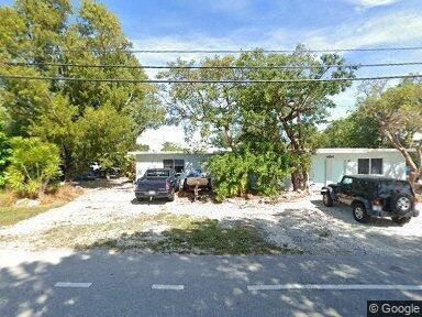 A gravel driveway leads to a house with a black car parked in front.