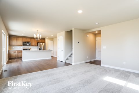 A spacious living room with a kitchen in the background and a carpet on the floor.