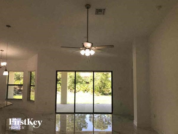 an empty living room with a ceiling fan and large windows