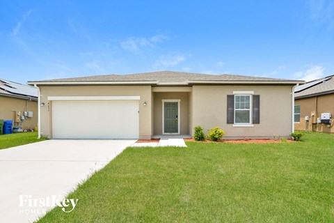A beige house with a garage door and a red brick pathway leading to the front door.
