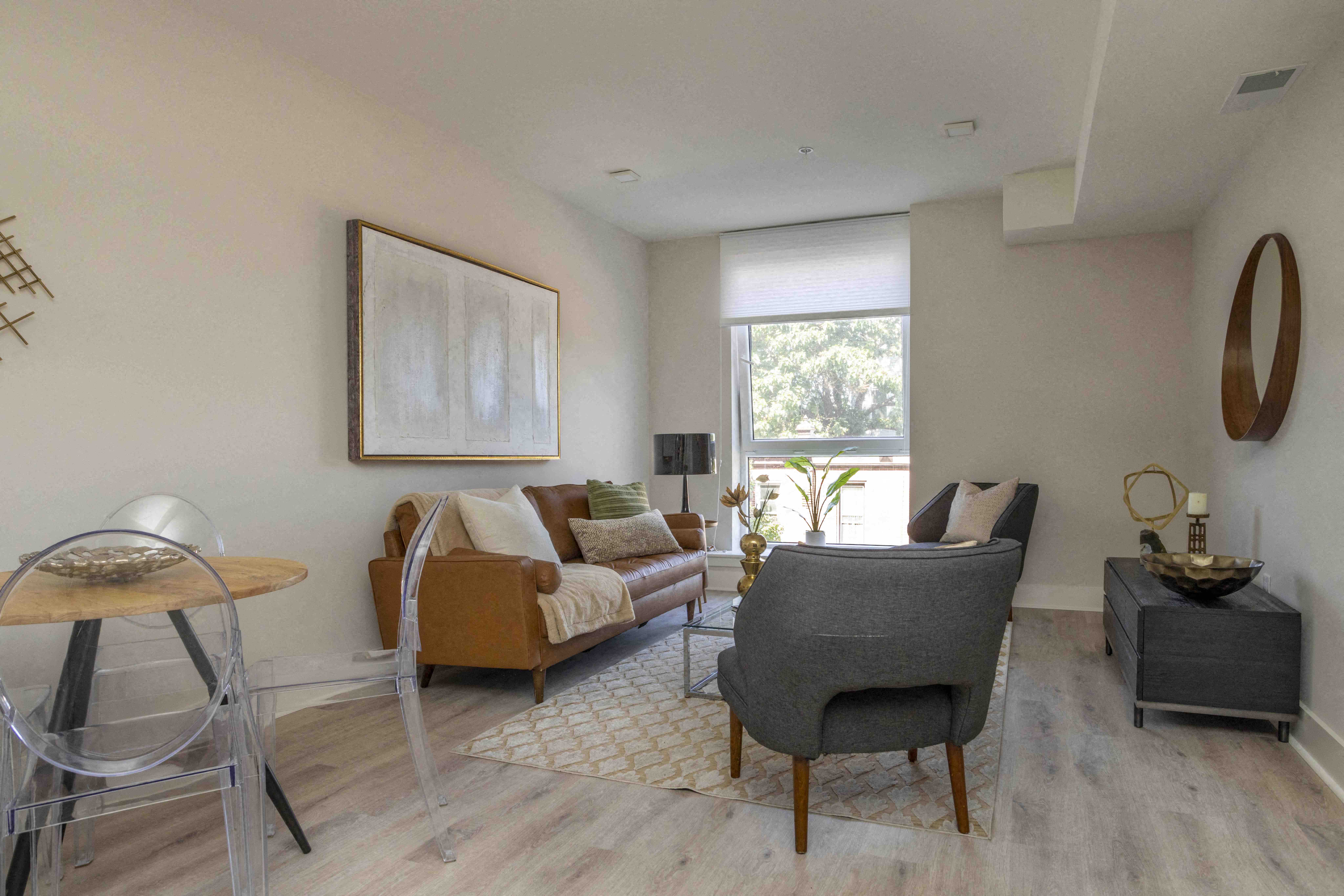 A living room with a grey armchair, a brown sofa, a wooden coffee table, and a large painting on the wall.