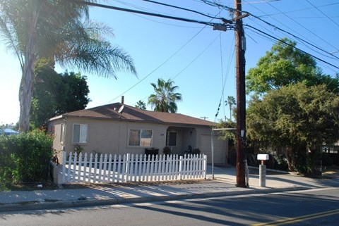 A house with a white picket fence is surrounded by trees and utility poles.