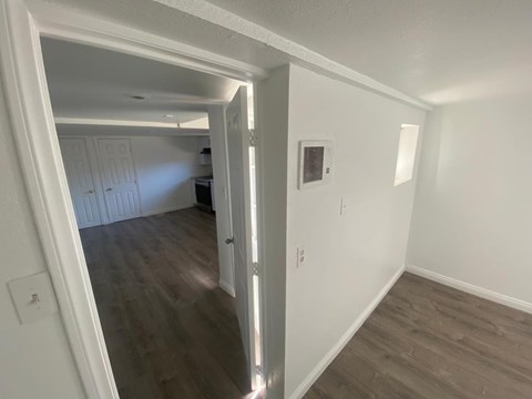 A room with white walls and wooden flooring with a doorway leading to another room.