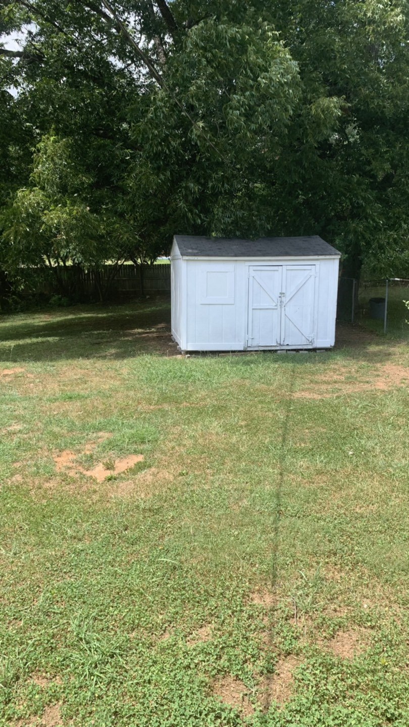 a small white shed in the middle of a grass field
