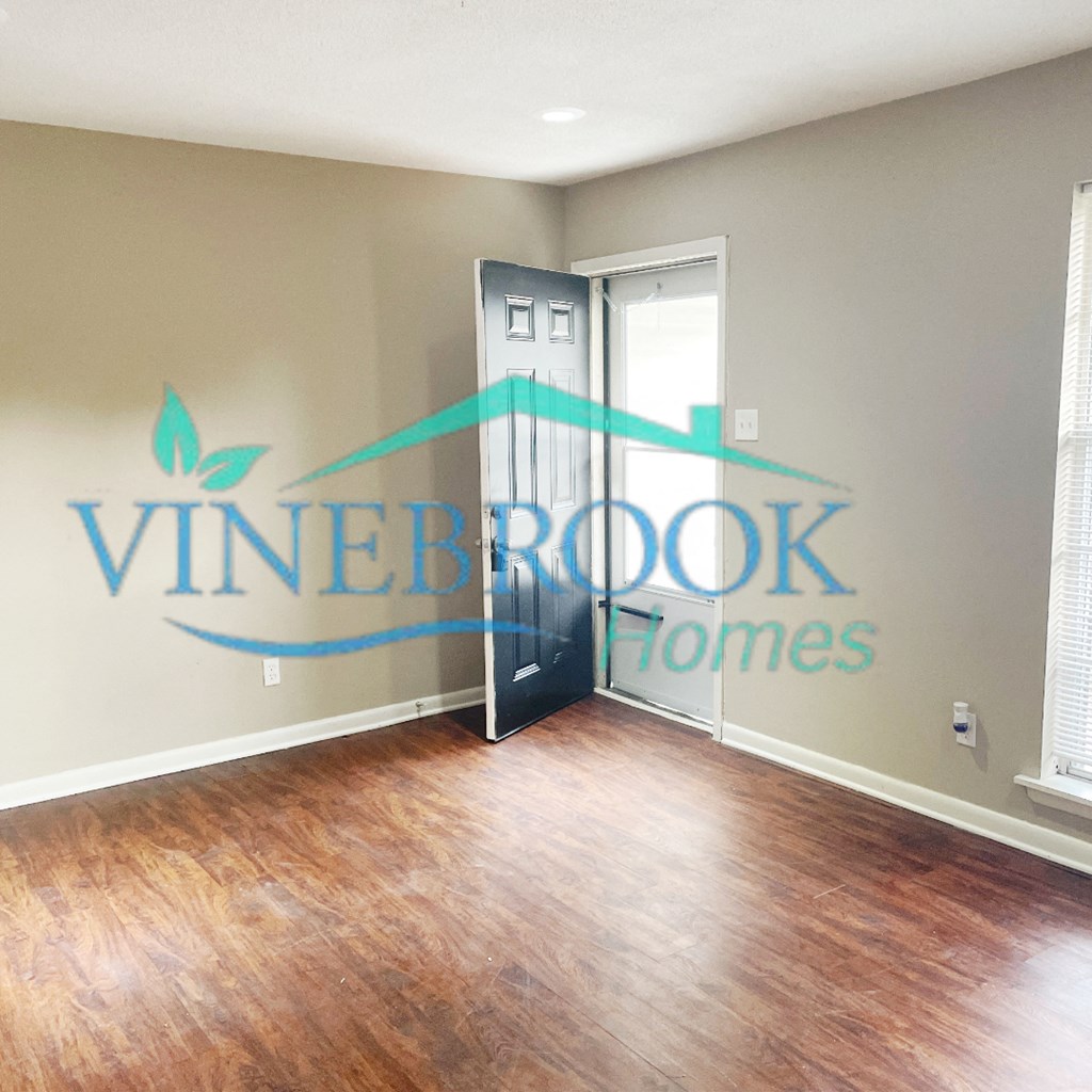 an empty living room with a hardwood floor and a door to a home office