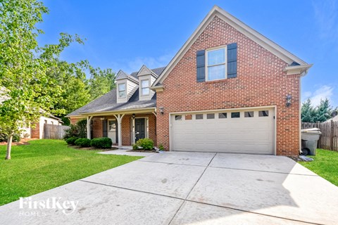 A brick house with a garage door and a tree in front.
