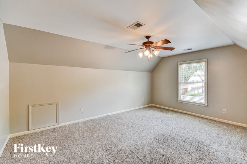 A room with a carpeted floor, a ceiling fan, and a window with blinds.