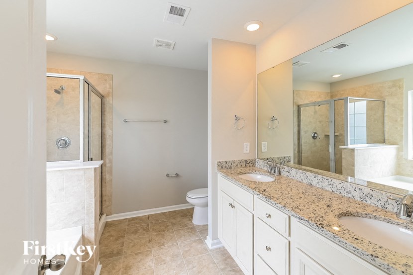 A bathroom with a walk-in shower, toilet, and double sinks.