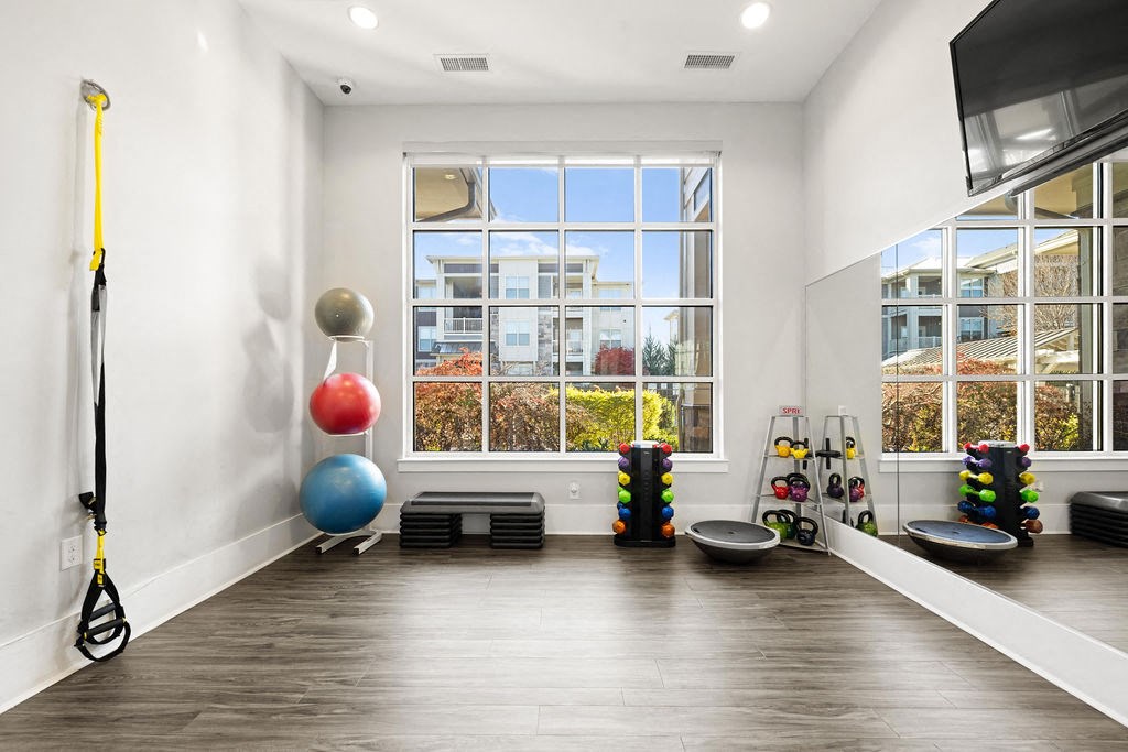 A room with a wooden floor and a large window with a view of buildings and trees outside.