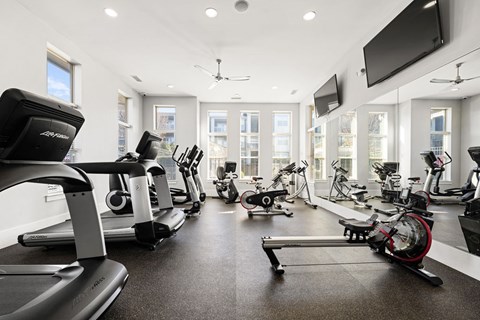 A spacious gym with treadmills, elliptical machines, and a television.