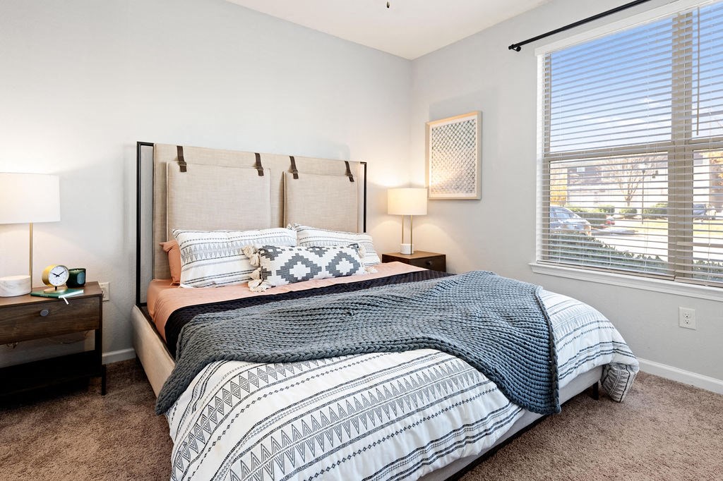 A bedroom with a large bed and a window with blinds.