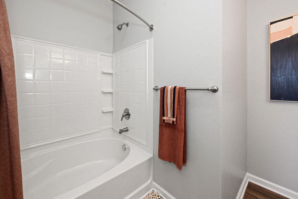 A white tiled bathroom with a white bathtub and a towel rack.