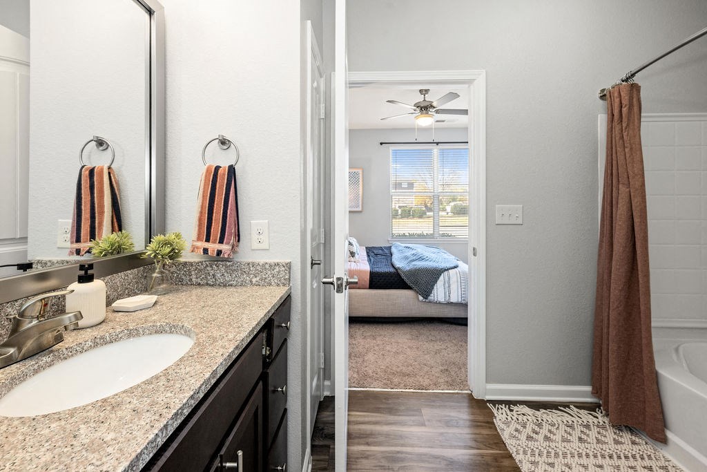 A bathroom with a large mirror, sink, and a view of a bedroom through the door.