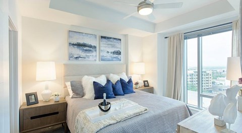 A bedroom with a large bed, a ceiling fan, and a view of the city.