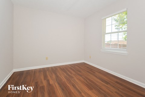 a bedroom with white walls and wood floors and a window