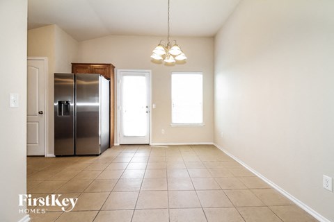 an empty dining room with a refrigerator and a door to the kitchen