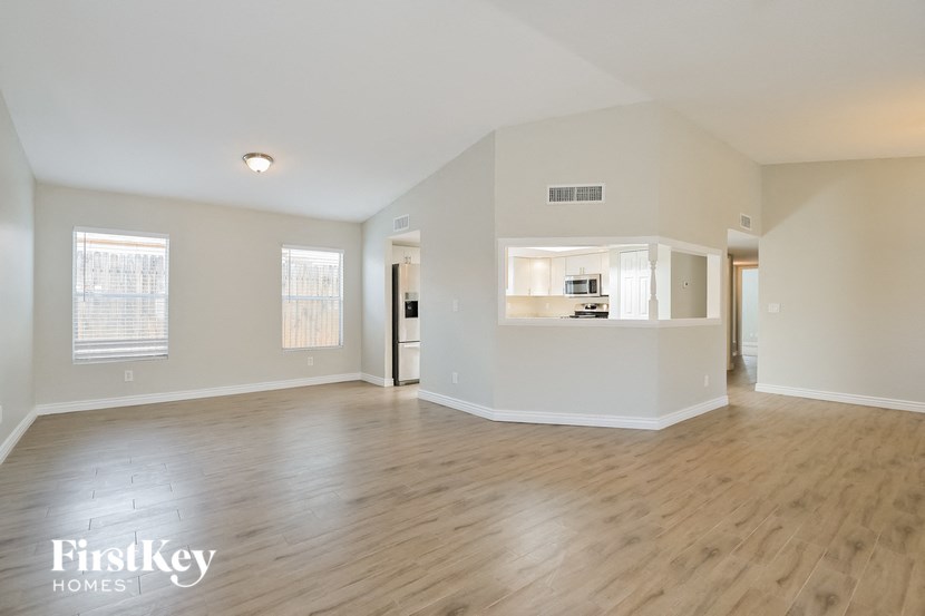 an empty living room with wood floors and a kitchen