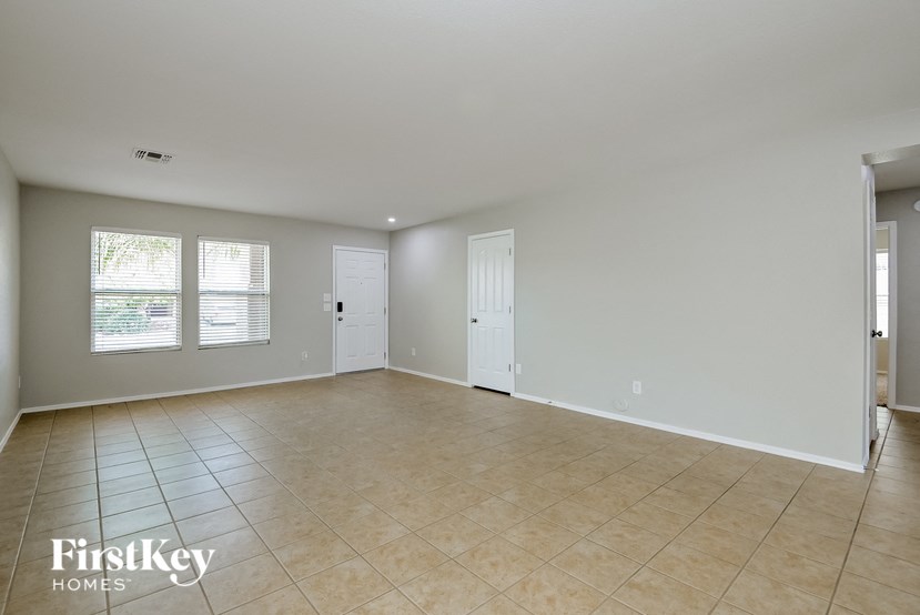 A spacious room with beige tiled flooring and white walls, with a door on the right and a window on the left.