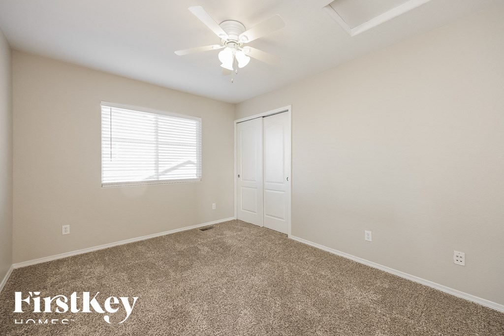 A room with a carpeted floor, a ceiling fan, and a window with blinds.