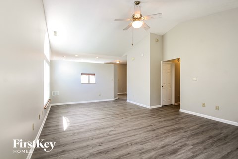 A spacious room with a ceiling fan and light fixture, and a doorway leading to another room.