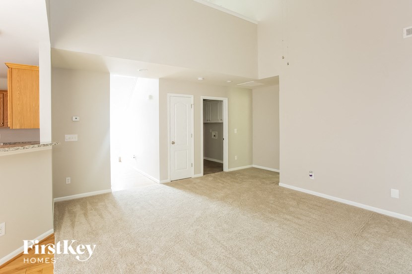 A spacious room with beige carpeting and a doorway leading to another room.